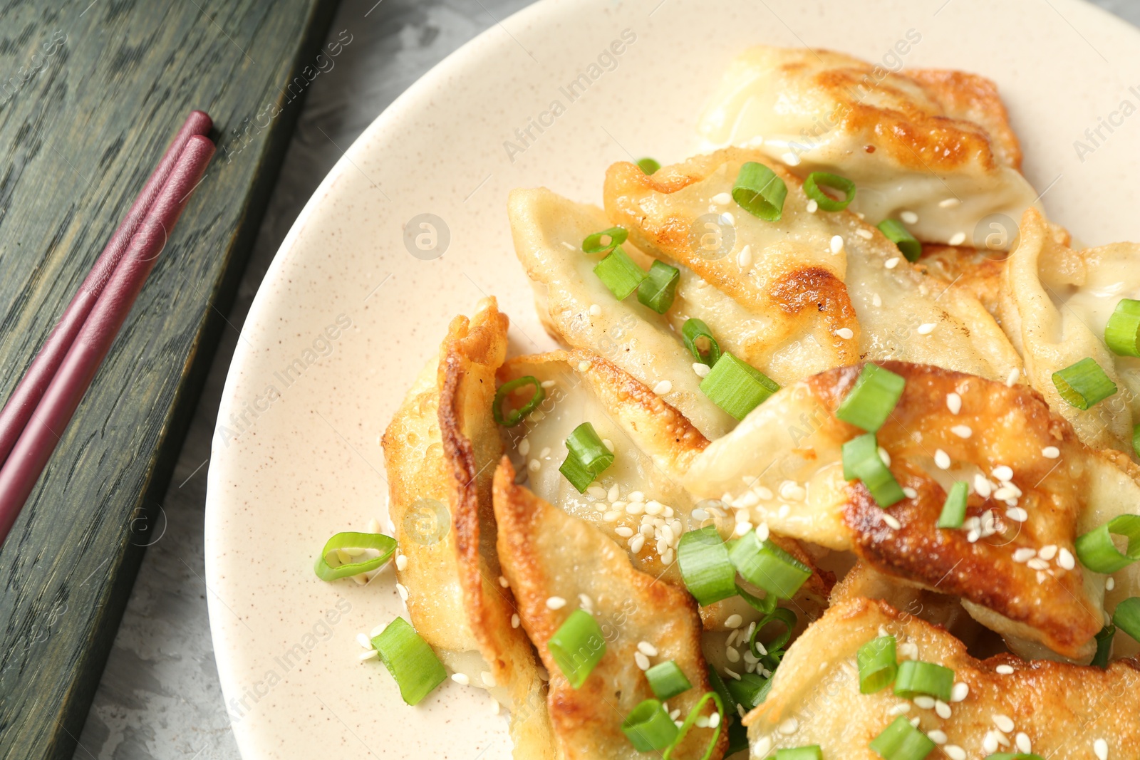 Photo of Tasty fried gyoza (dumplings) and chopsticks on light grey table, top view