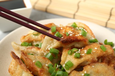 Photo of Taking tasty fried gyoza (dumpling) with chopsticks at table, closeup