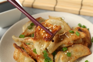 Photo of Taking tasty fried gyoza (dumpling) with chopsticks at table, closeup