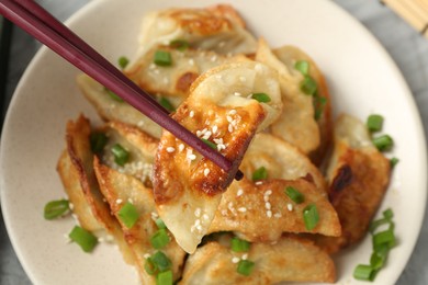 Photo of Taking tasty fried gyoza (dumpling) with chopsticks at table, top view