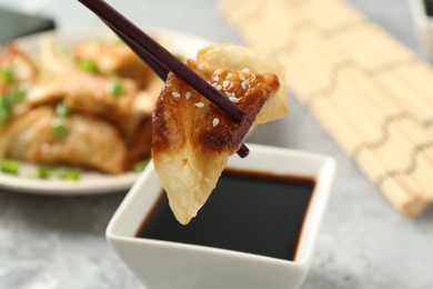 Photo of Taking tasty fried gyoza (dumpling) with chopsticks at light grey table, closeup