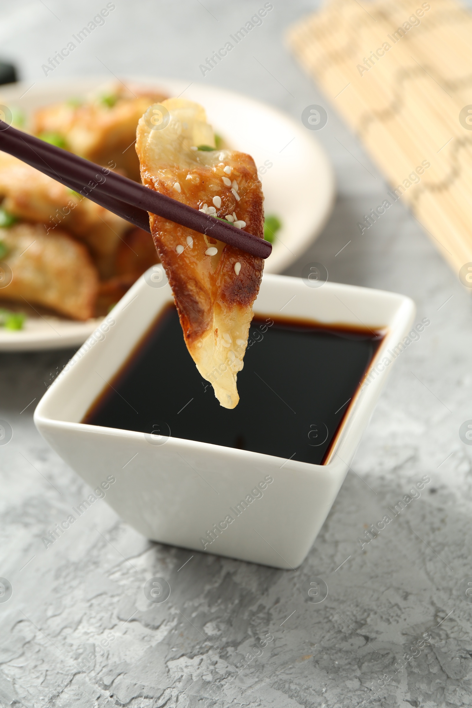 Photo of Taking tasty fried gyoza (dumpling) with chopsticks at light grey table, closeup