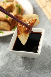 Photo of Taking tasty fried gyoza (dumpling) with chopsticks at light grey table, closeup