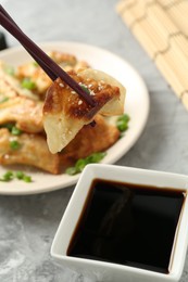 Photo of Taking tasty fried gyoza (dumpling) with chopsticks at light grey table, closeup