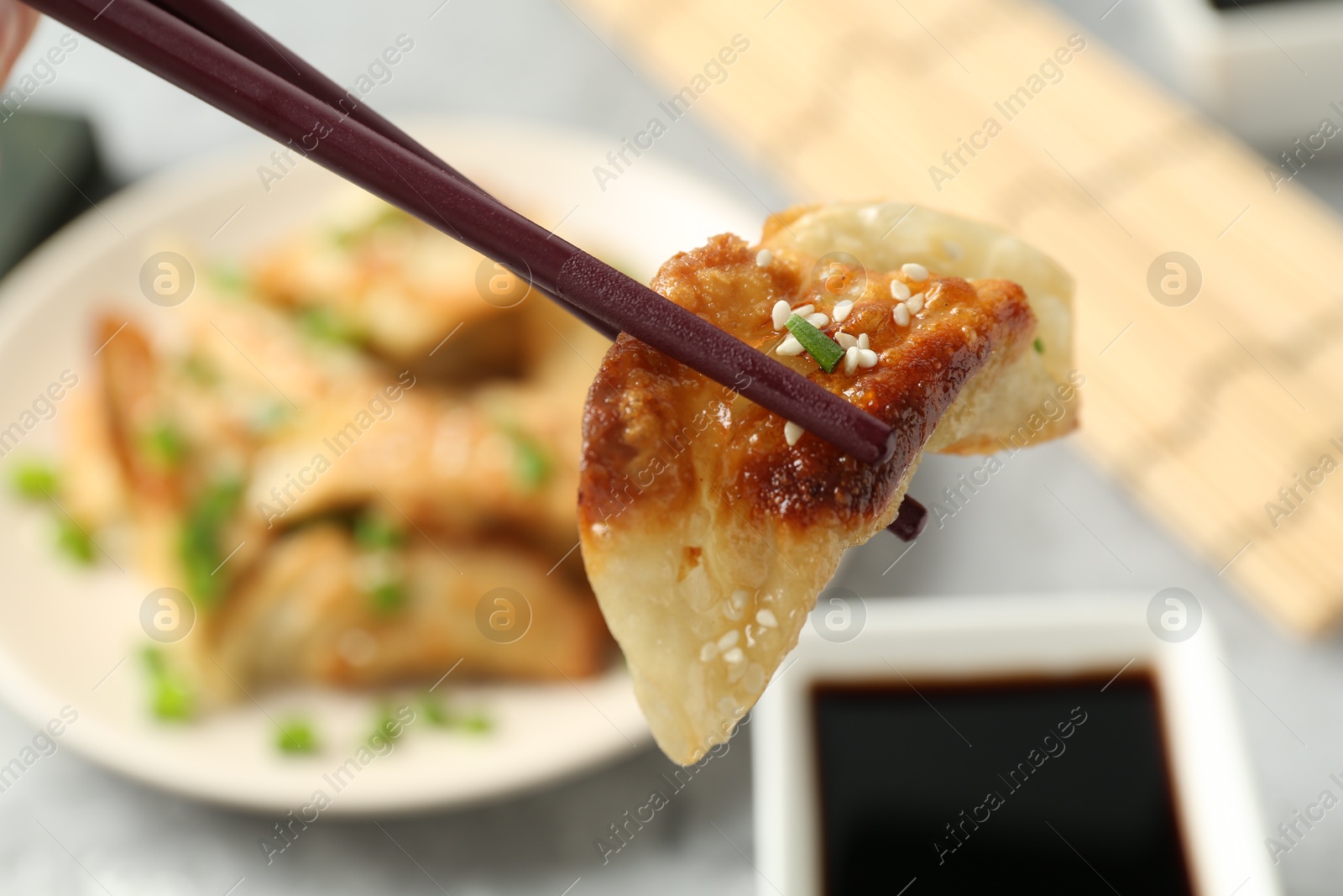 Photo of Taking tasty fried gyoza (dumpling) with chopsticks at light grey table, closeup