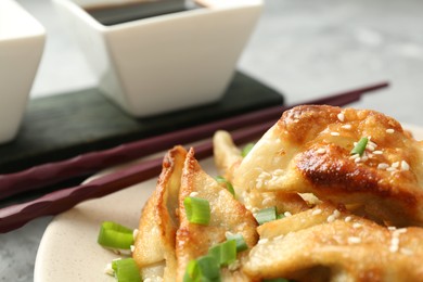 Photo of Tasty fried gyoza (dumplings), soy sauce and chopsticks on light grey table, closeup