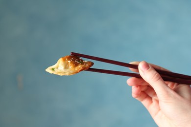 Photo of Woman holding tasty fried gyoza (dumpling) with chopsticks on light blue background, closeup