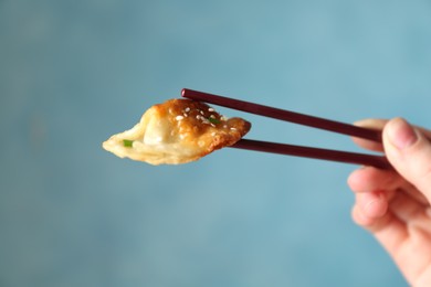 Photo of Woman holding tasty fried gyoza (dumpling) with chopsticks on light blue background, closeup