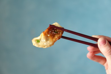 Photo of Woman holding tasty fried gyoza (dumpling) with chopsticks on light blue background, closeup