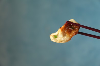 Photo of Holding tasty fried gyoza (dumpling) with chopsticks on light blue background, closeup. Space for text