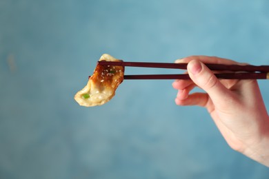 Photo of Woman holding tasty fried gyoza (dumpling) with chopsticks on light blue background, closeup