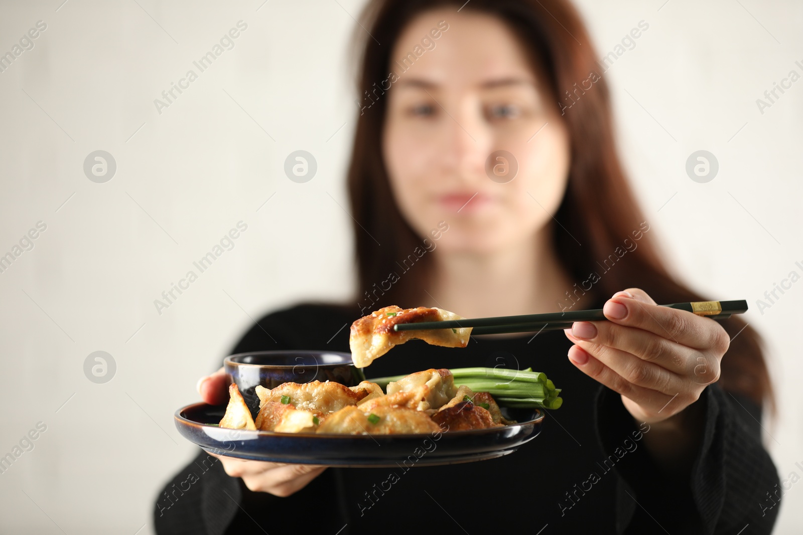 Photo of Woman holding tasty fried gyoza (dumplings) on white background, selective focus