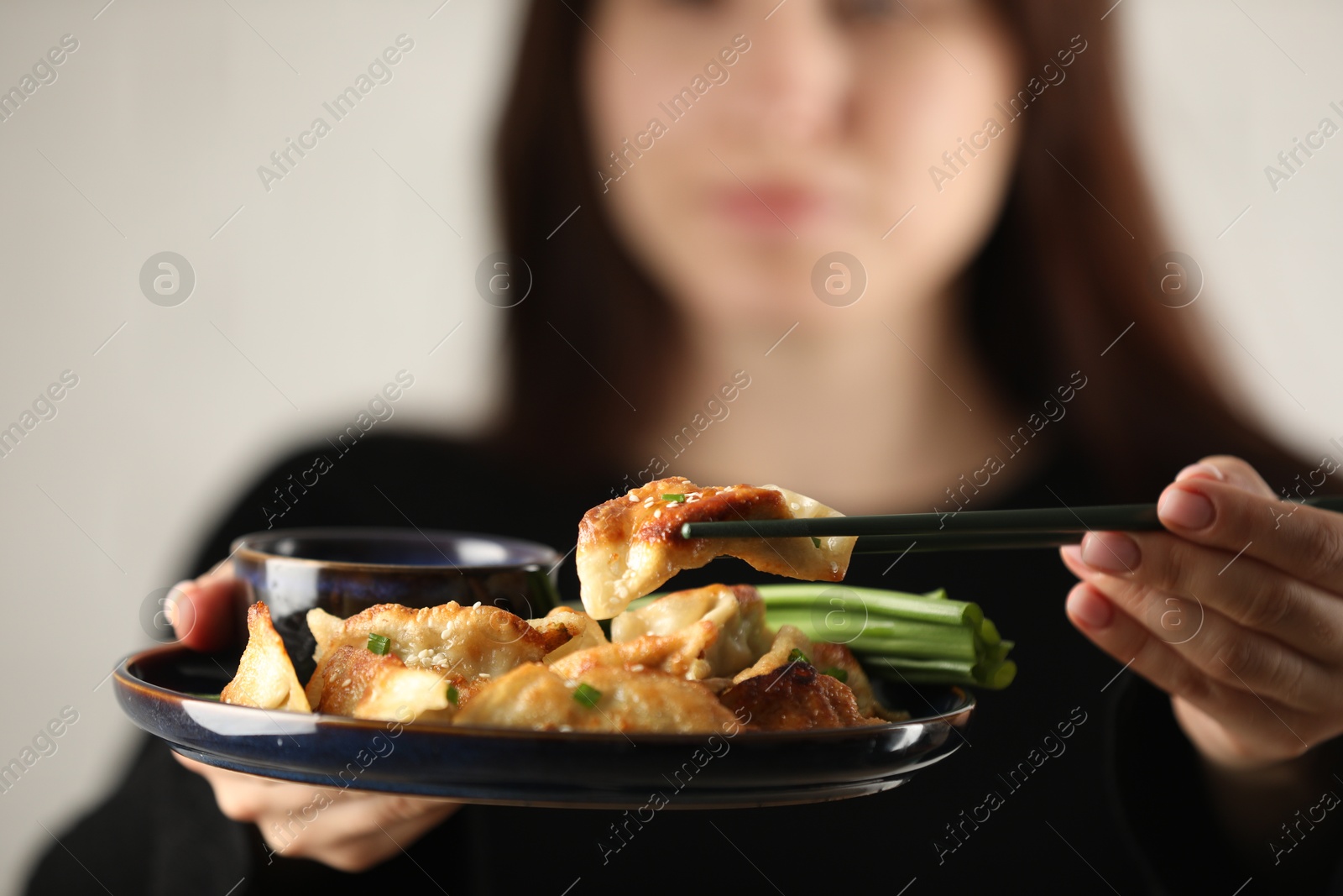 Photo of Woman holding tasty fried gyoza (dumplings) on white background, selective focus