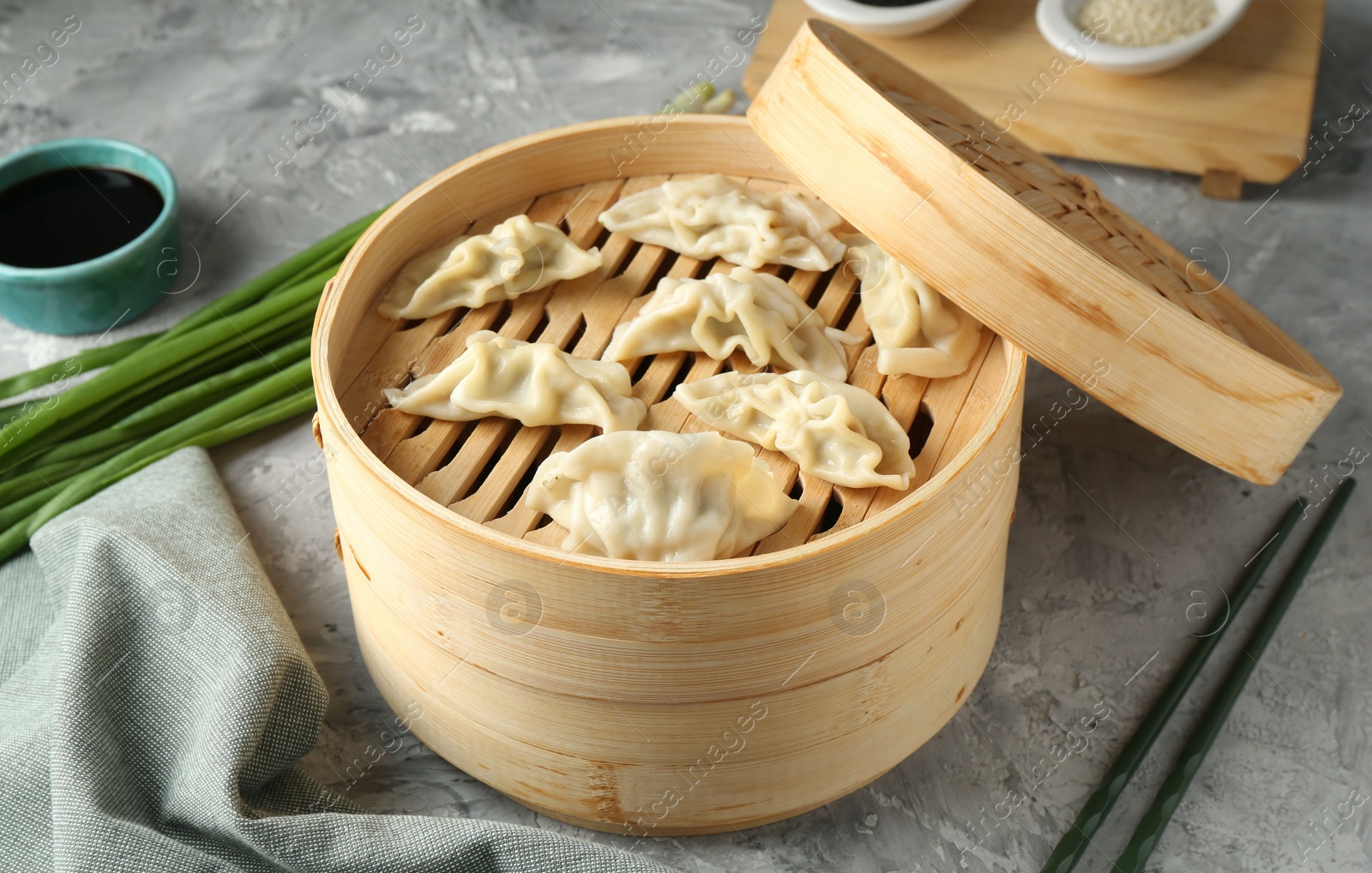 Photo of Tasty boiled gyoza (dumplings) in bamboo steamer on light grey table, closeup