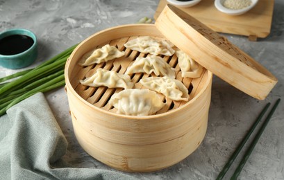 Photo of Tasty boiled gyoza (dumplings) in bamboo steamer on light grey table, closeup