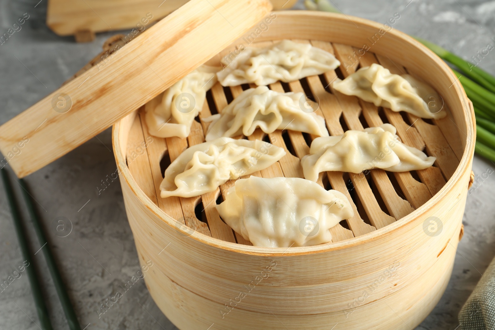 Photo of Tasty boiled gyoza (dumplings) in bamboo steamer on light grey table, closeup