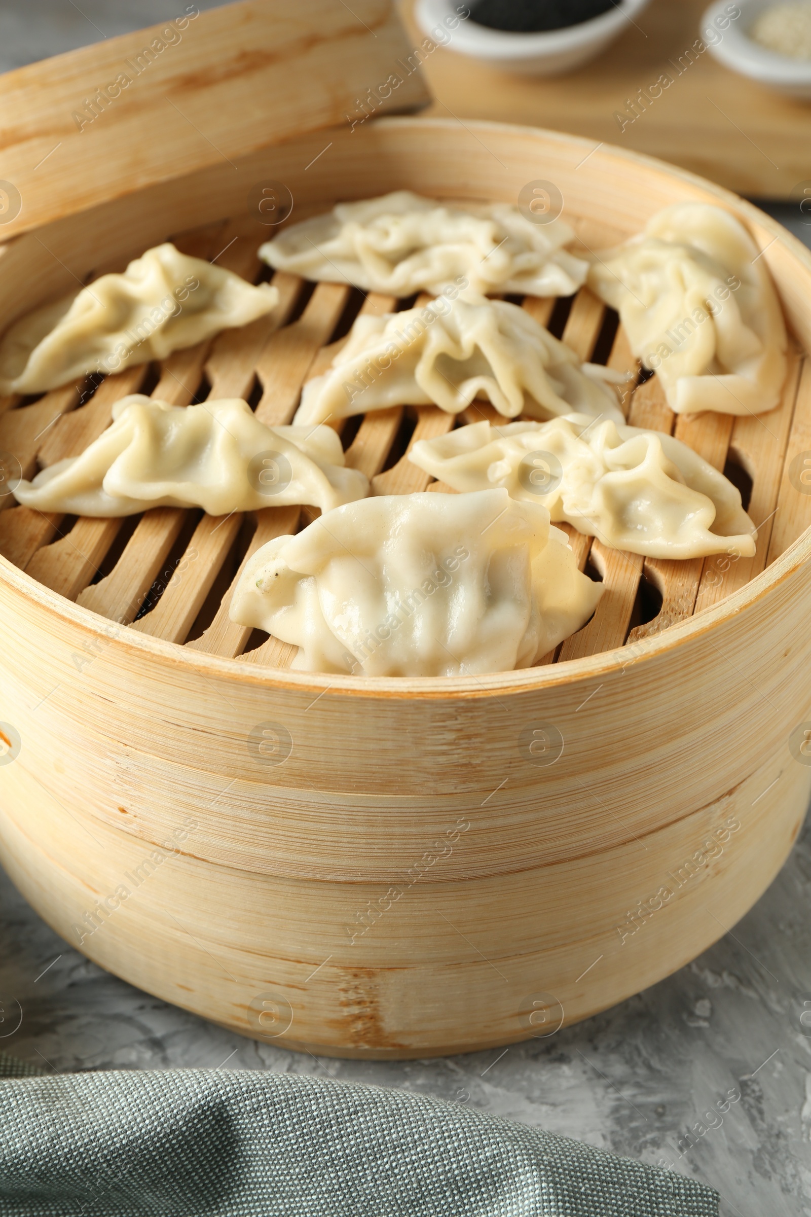 Photo of Tasty boiled gyoza (dumplings) in bamboo steamer on light grey table, closeup