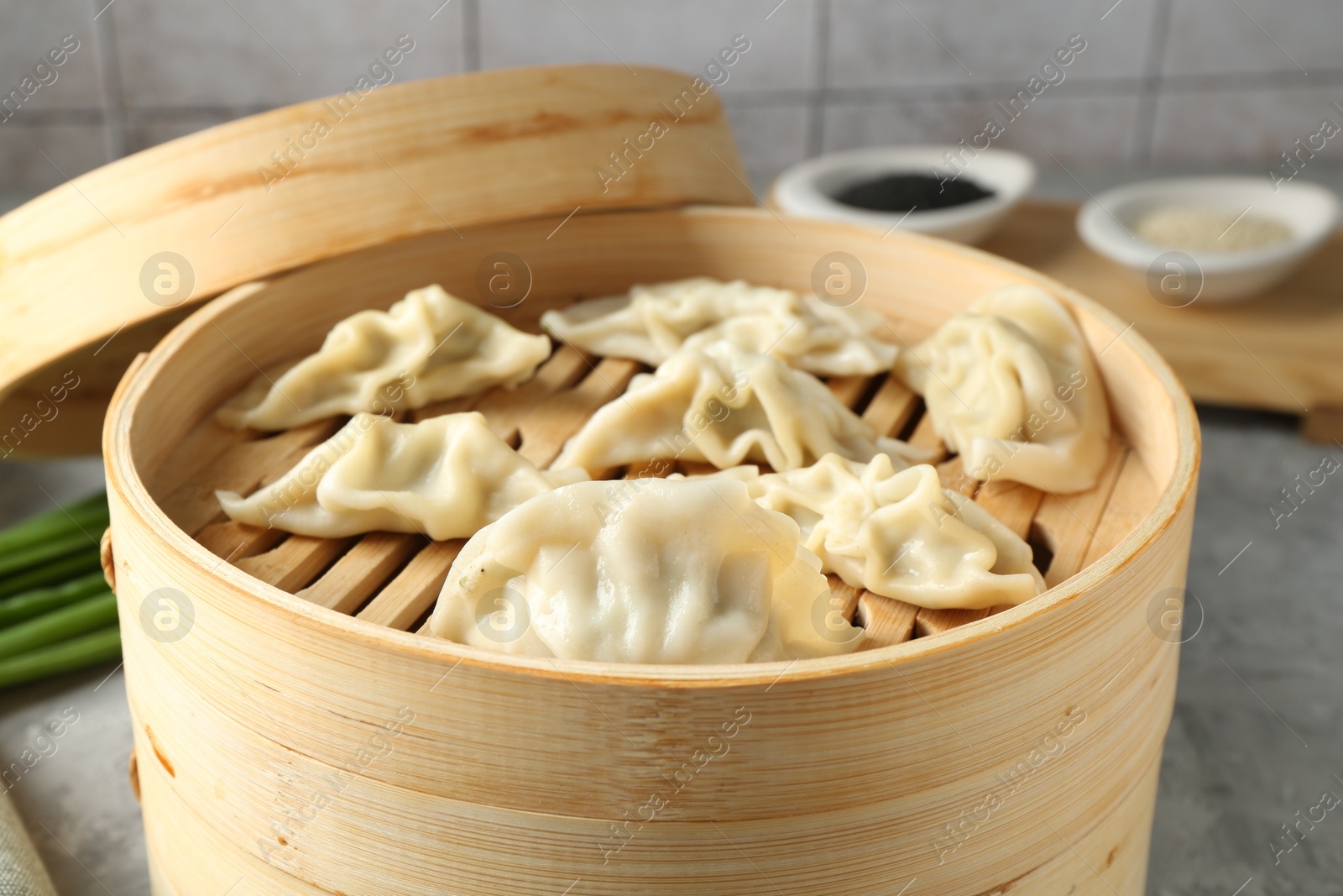 Photo of Tasty boiled gyoza (dumplings) in bamboo steamer on light grey table, closeup