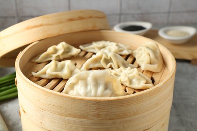 Photo of Tasty boiled gyoza (dumplings) in bamboo steamer on light grey table, closeup