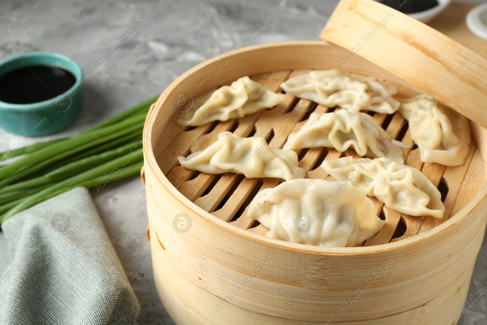 Photo of Tasty boiled gyoza (dumplings) in bamboo steamer on light grey table, closeup