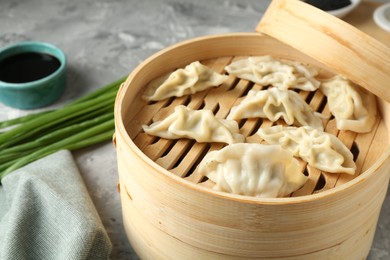 Photo of Tasty boiled gyoza (dumplings) in bamboo steamer on light grey table, closeup