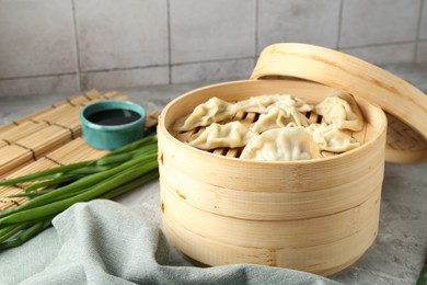 Photo of Tasty boiled gyoza (dumplings) in bamboo steamer on light grey table, closeup