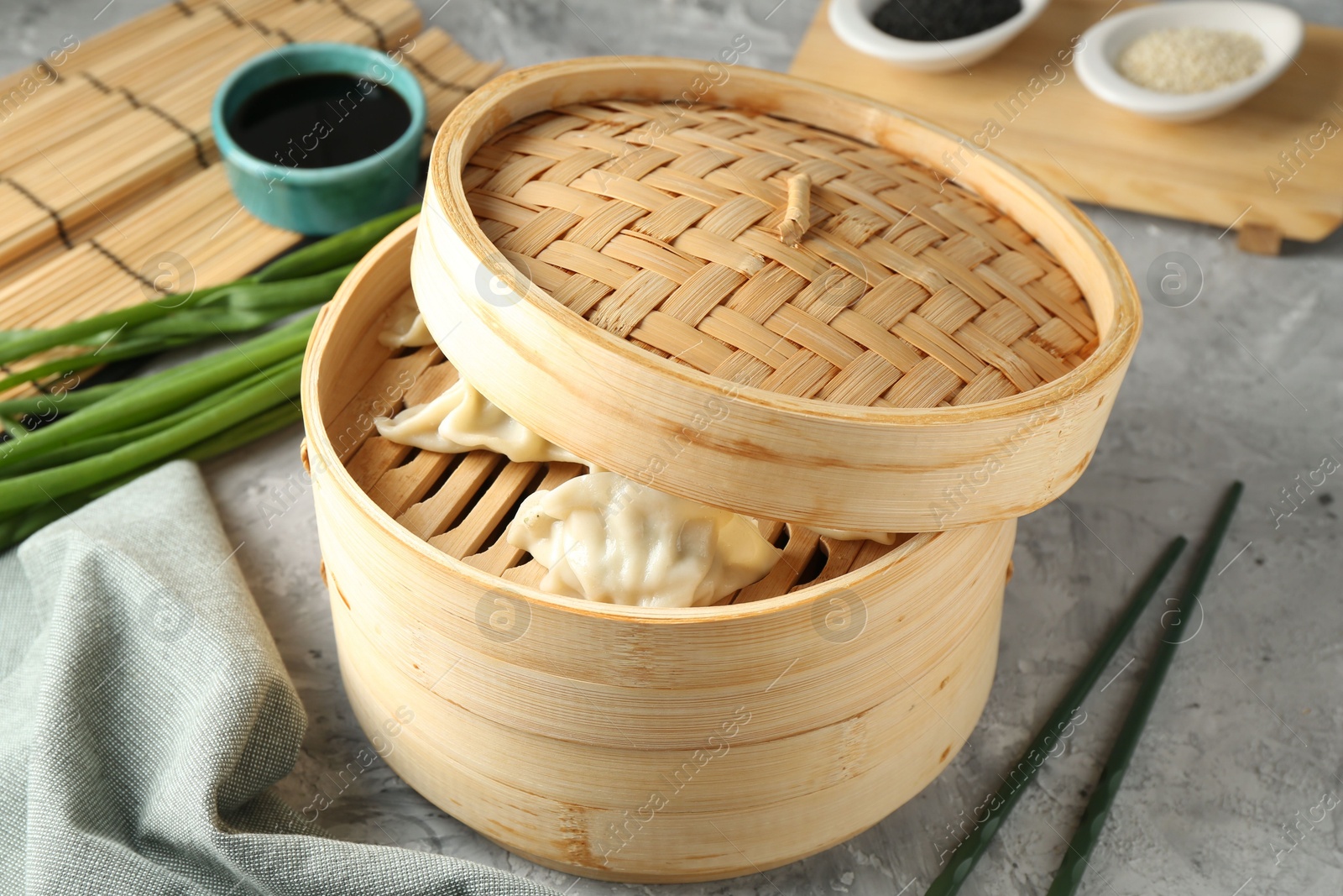 Photo of Tasty boiled gyoza (dumplings) in bamboo steamer on light grey table, closeup