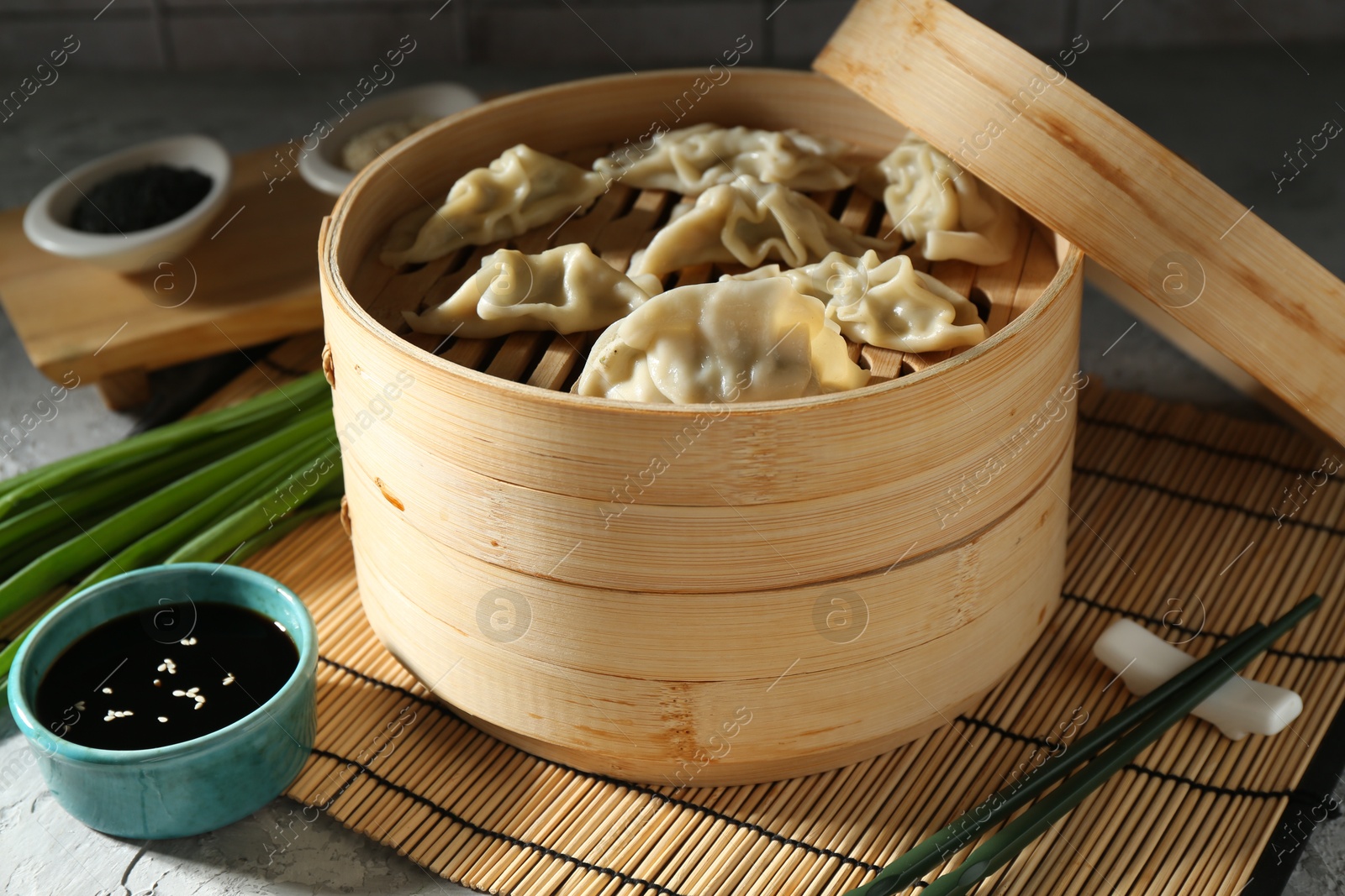 Photo of Tasty boiled gyoza (dumplings) in bamboo steamer on light grey table, closeup