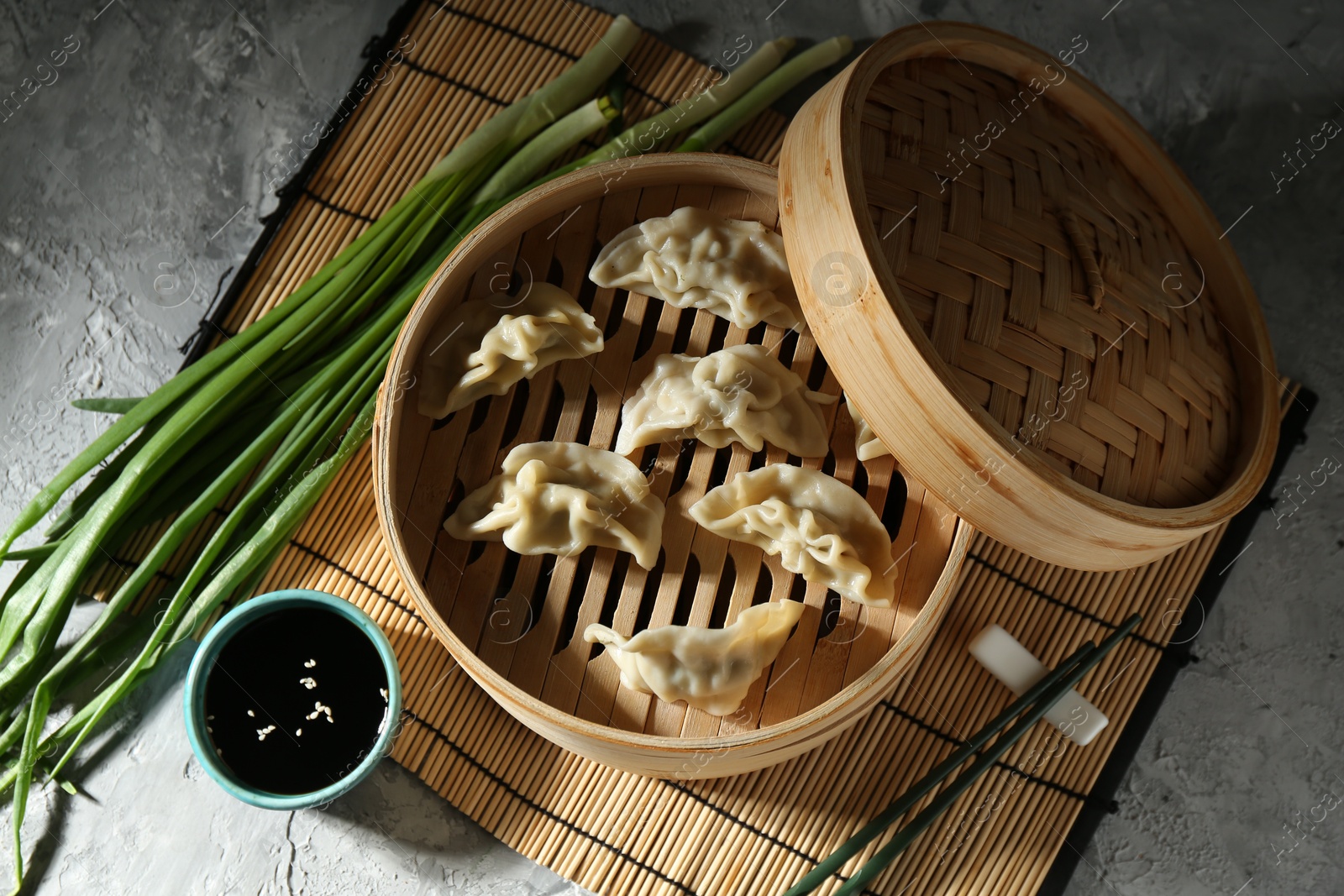 Photo of Tasty boiled gyoza (dumplings) in bamboo steamer and soy sauce on light grey table, flat lay