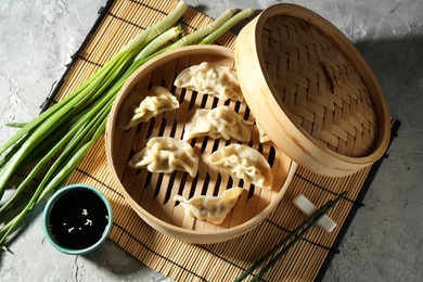 Photo of Tasty boiled gyoza (dumplings) in bamboo steamer and soy sauce on light grey table, flat lay