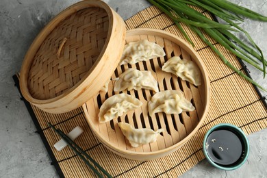 Photo of Tasty boiled gyoza (dumplings) in bamboo steamer and soy sauce on light grey table, flat lay