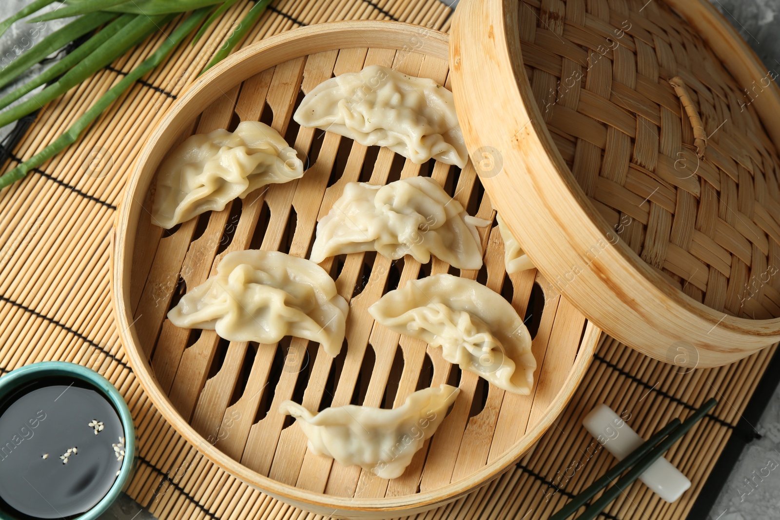 Photo of Tasty boiled gyoza (dumplings) in bamboo steamer and soy sauce on light grey table, flat lay