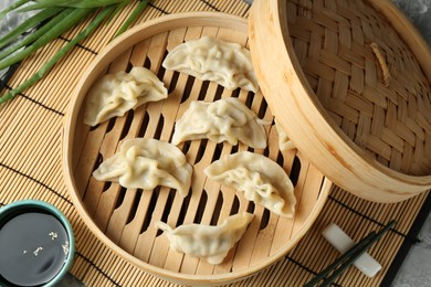 Photo of Tasty boiled gyoza (dumplings) in bamboo steamer and soy sauce on light grey table, flat lay