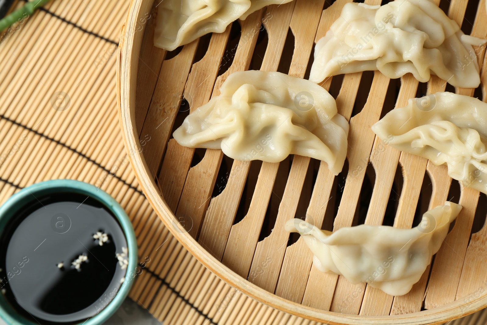 Photo of Tasty boiled gyoza (dumplings) in bamboo steamer and soy sauce on table, flat lay