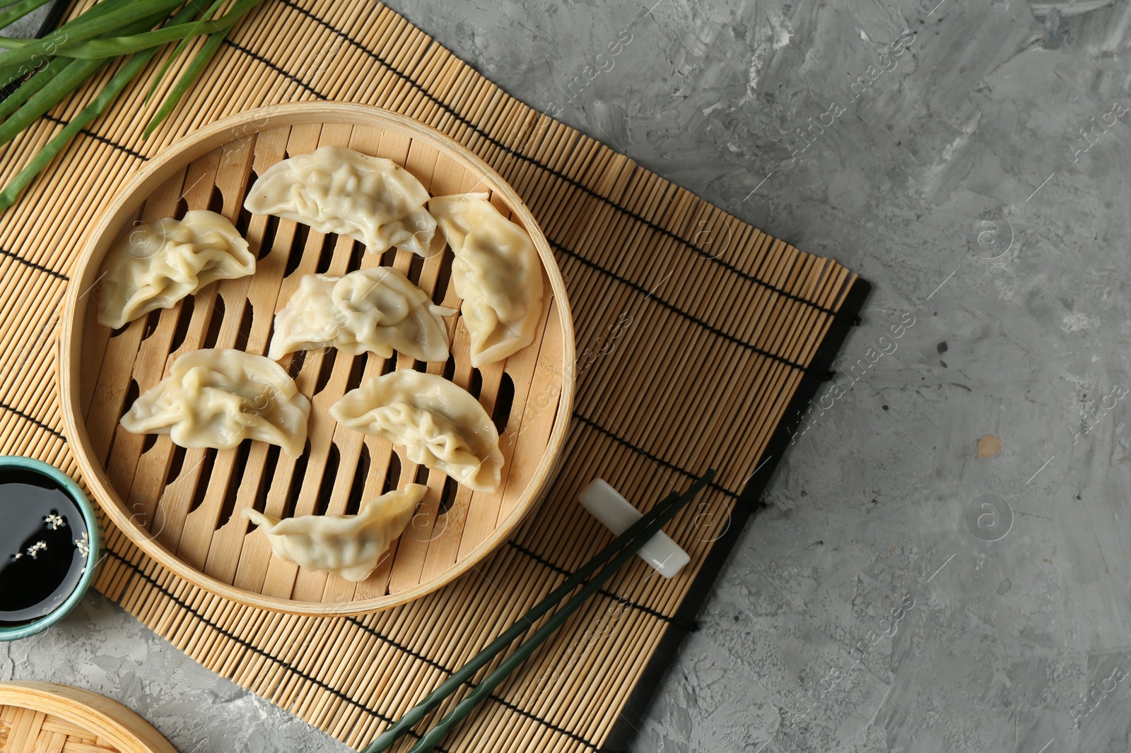 Photo of Tasty boiled gyoza (dumplings) in bamboo steamer on light grey table, flat lay. Space for text