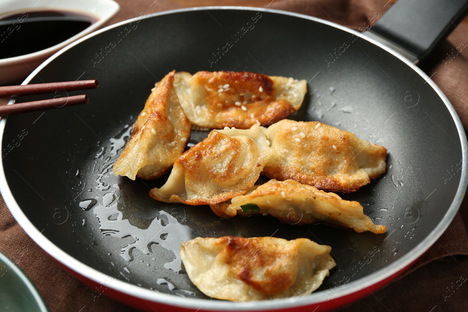 Photo of Tasty fried gyoza (dumplings) in frying pan on wooden table, closeup