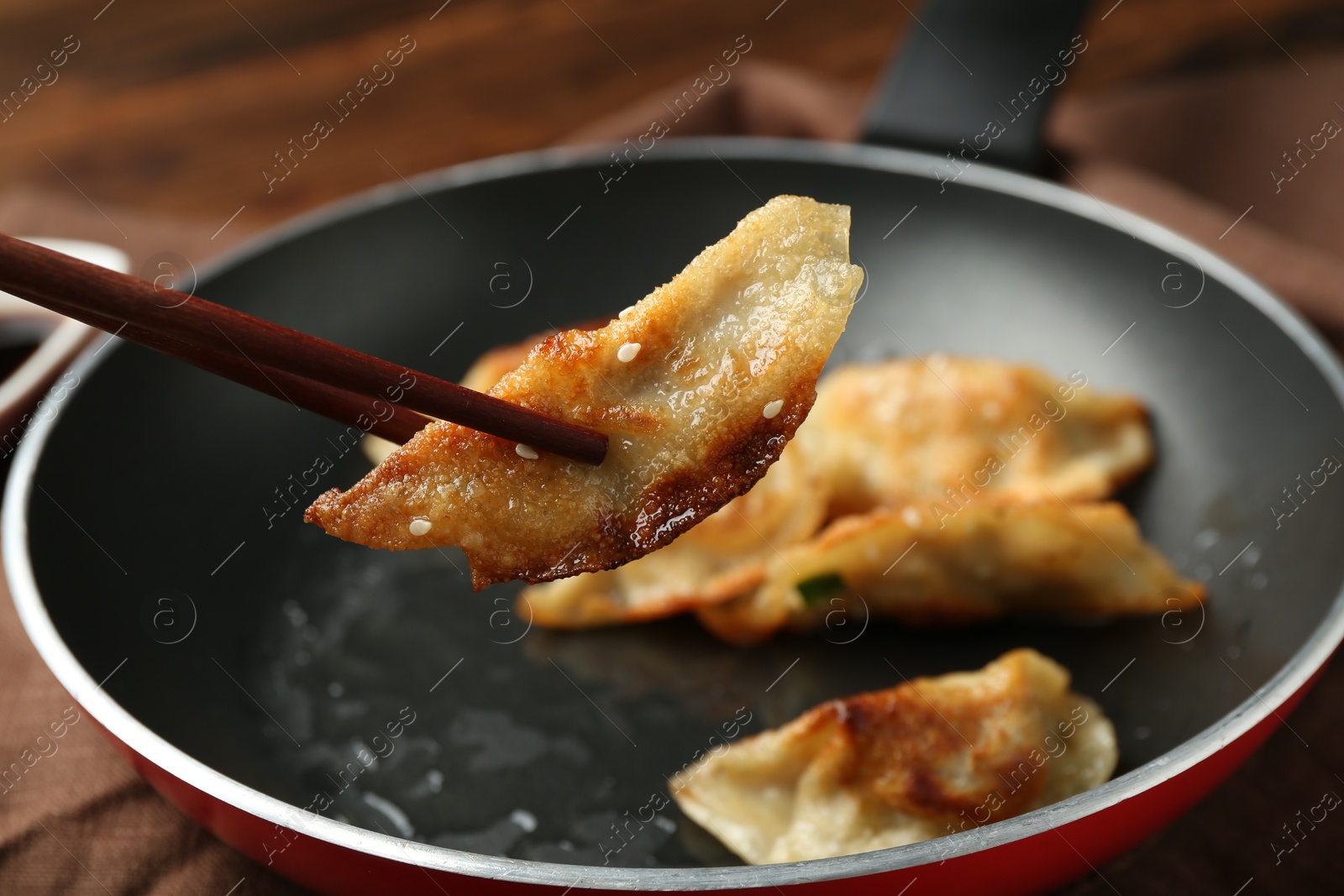 Photo of Taking tasty fried gyoza (dumpling) with chopsticks on wooden table, closeup