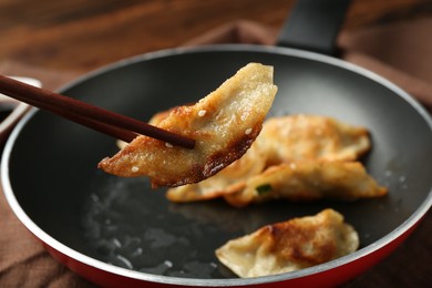 Photo of Taking tasty fried gyoza (dumpling) with chopsticks on wooden table, closeup