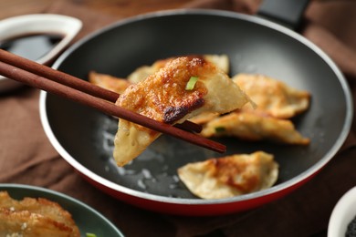 Photo of Taking tasty fried gyoza (dumpling) with chopsticks on wooden table, closeup