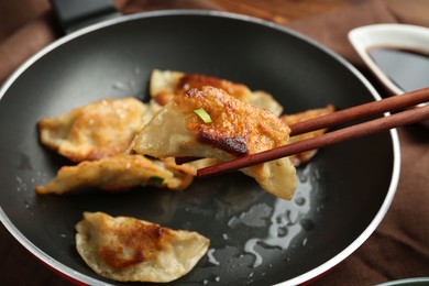 Photo of Taking tasty fried gyoza (dumpling) with chopsticks on wooden table, closeup