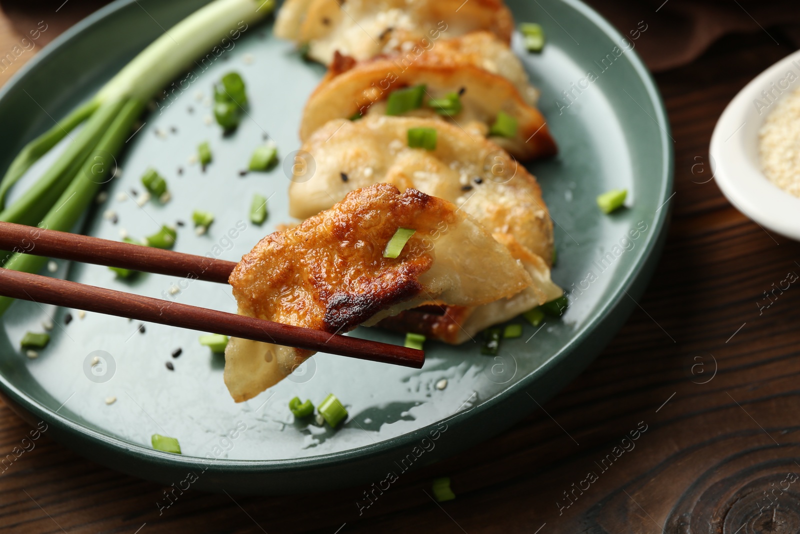 Photo of Taking tasty fried gyoza (dumpling) with chopsticks on wooden table, closeup