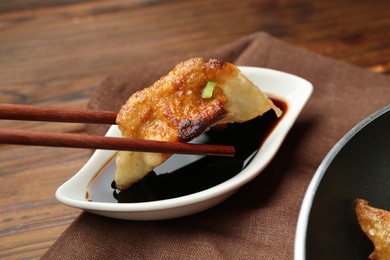 Photo of Dipping tasty fried gyoza (dumpling) into soy sauce on wooden table, closeup