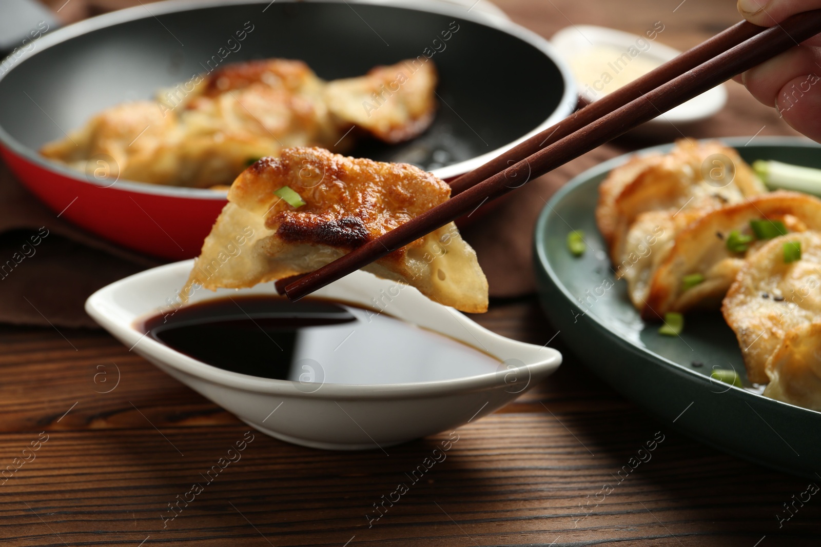 Photo of Dipping tasty fried gyoza (dumpling) into soy sauce on wooden table, closeup