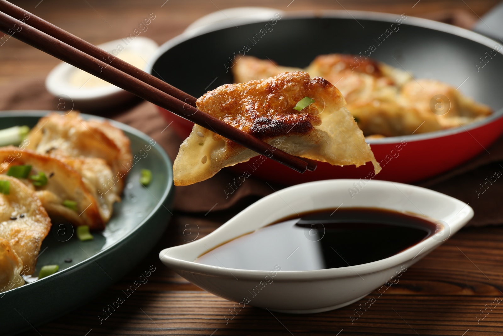 Photo of Dipping tasty fried gyoza (dumpling) into soy sauce on wooden table, closeup