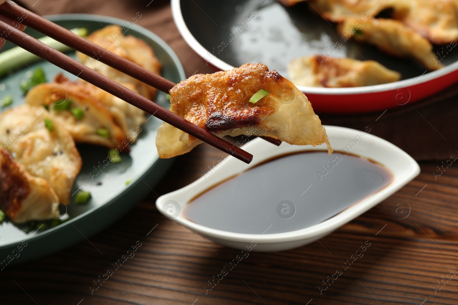 Photo of Dipping tasty fried gyoza (dumpling) into soy sauce on wooden table, closeup