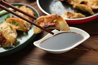 Photo of Dipping tasty fried gyoza (dumpling) into soy sauce on wooden table, closeup