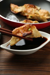 Photo of Dipping tasty fried gyoza (dumpling) into soy sauce on wooden table, closeup