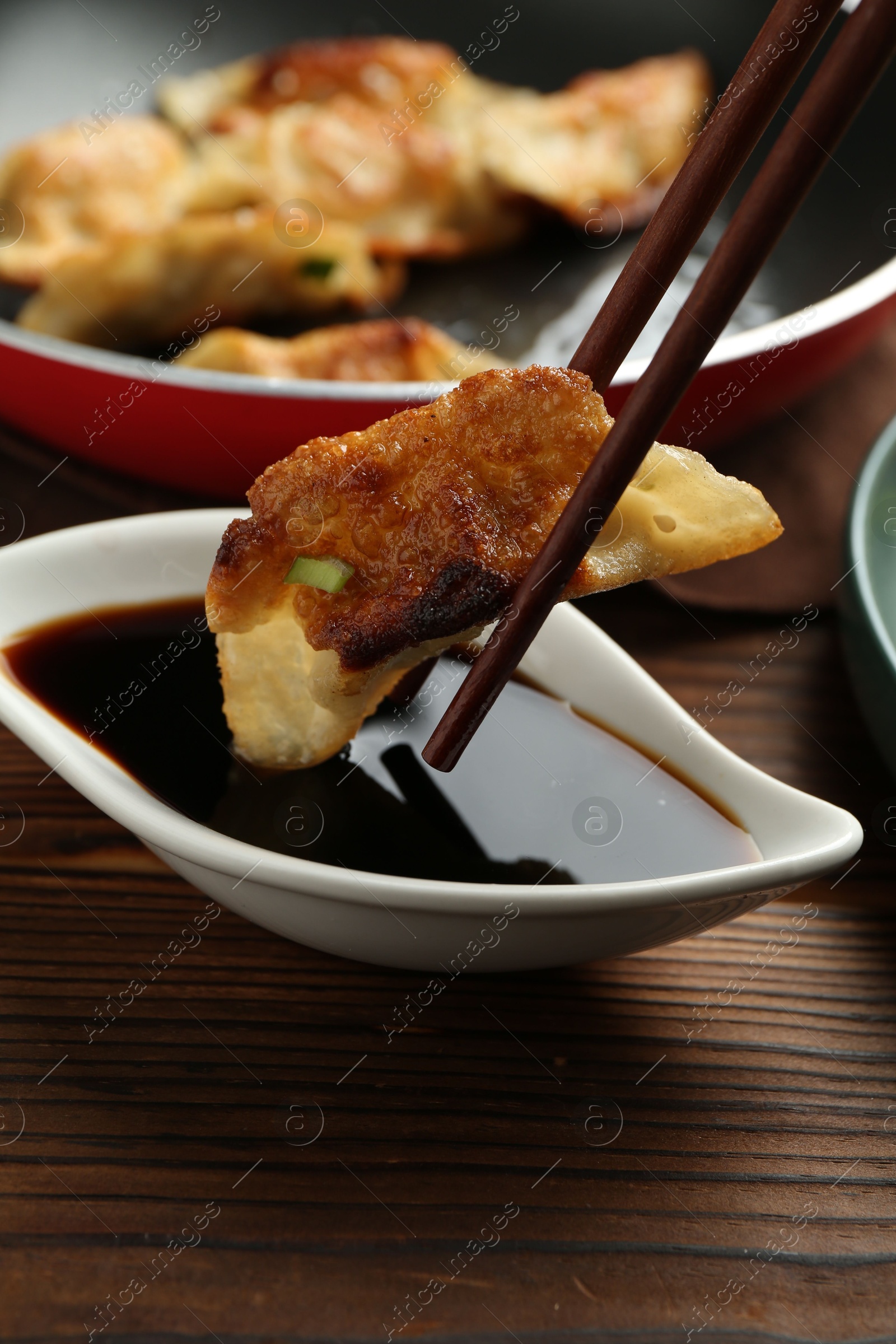 Photo of Dipping tasty fried gyoza (dumpling) into soy sauce on wooden table, closeup