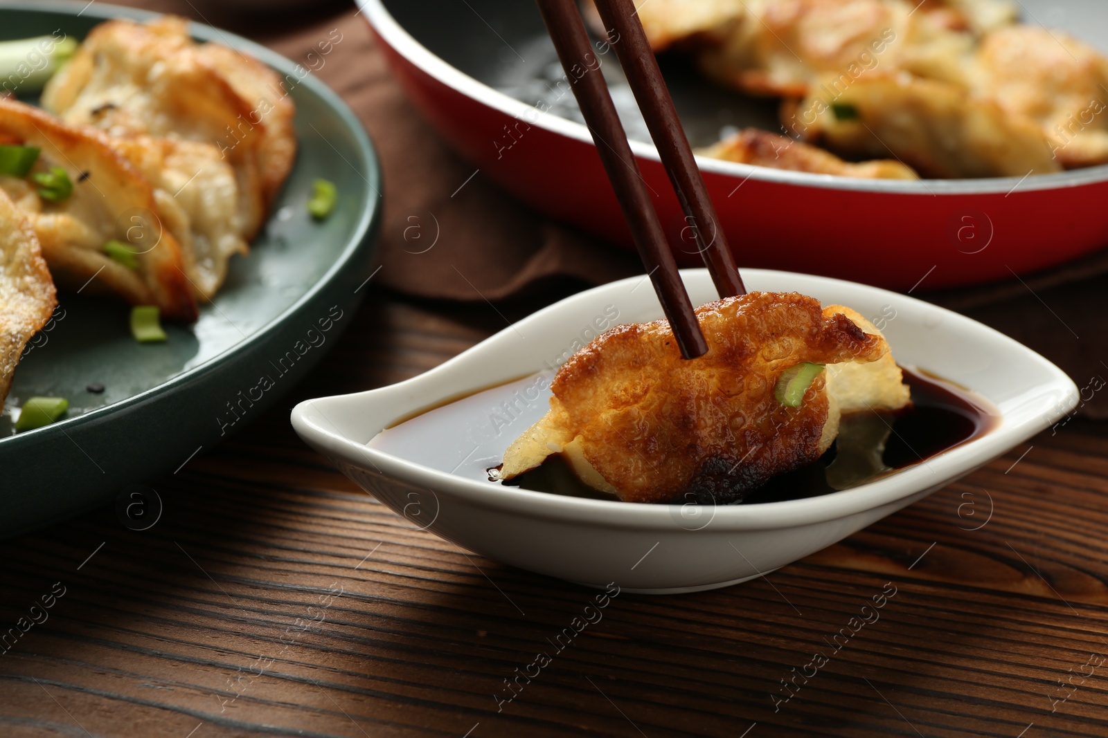 Photo of Dipping tasty fried gyoza (dumpling) into soy sauce on wooden table, closeup