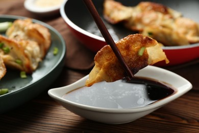 Photo of Dipping tasty fried gyoza (dumpling) into soy sauce on wooden table, closeup